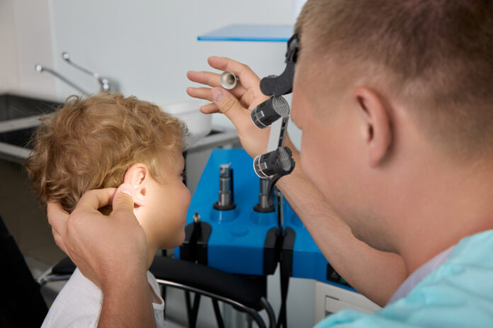 experienced doctor uses headlamp and medical instruments examine ears curly boy